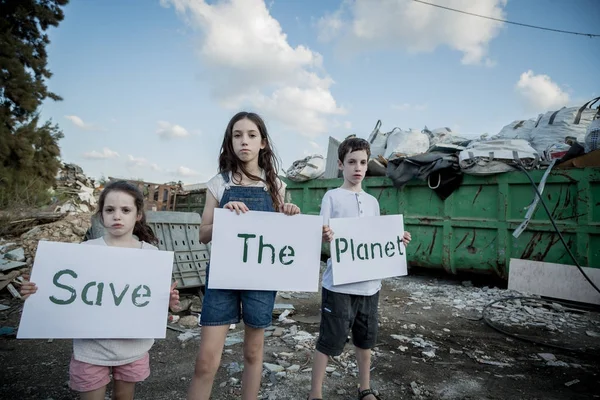 Save the planet. young kids holding signs standing in a huge junkyard