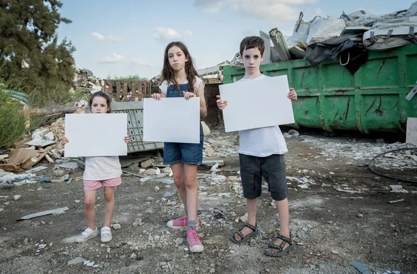 Save the planet. young kids holding signs standing in a huge junkyard