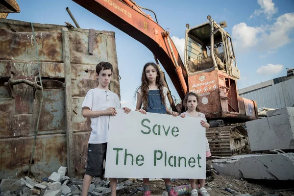 Save the planet. young kids holding signs standing in a huge junkyard