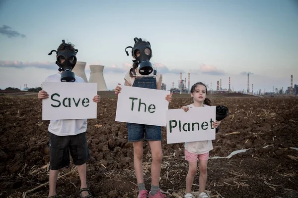 Gezegeni kurtar. Gaz maskeleri ile bir rafineri yakınında duran işaretler tutan genç çocuklar