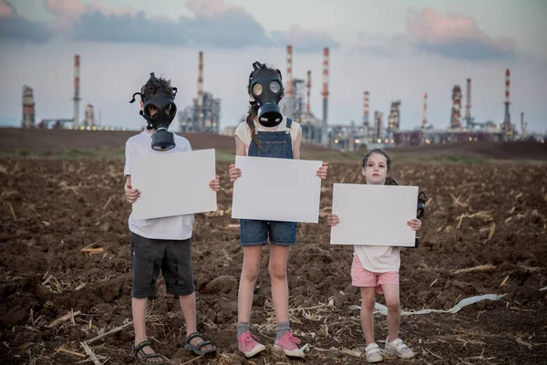 Gezegeni kurtar. Gaz maskeleri ile bir rafineri yakınında duran işaretler tutan genç çocuklar