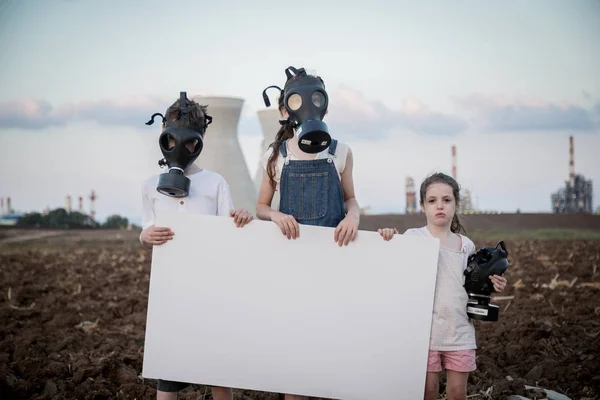Gezegeni kurtar. Gaz maskeleri ile bir rafineri yakınında duran işaretler tutan genç çocuklar
