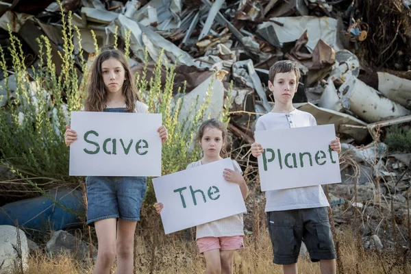 Rädda planeten. unga barn hålla tecken står i en enorm skroten Stockbild
