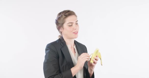 Жінка їсть банан на білому фоні студії — стокове відео