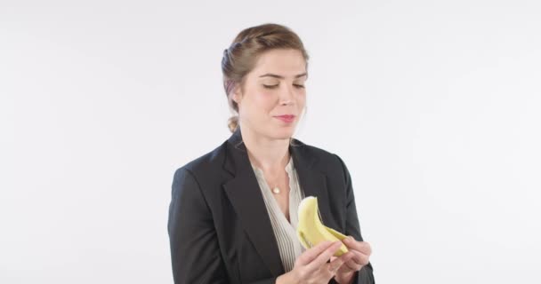 Mujer pelando y comiendo un plátano en un fondo de estudio blanco — Vídeo de stock