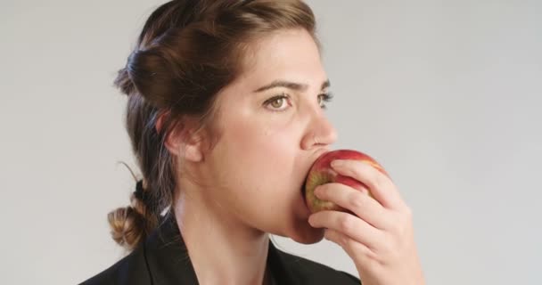 Mulher comendo uma grande maçã vermelha em um fundo de estúdio branco — Vídeo de Stock