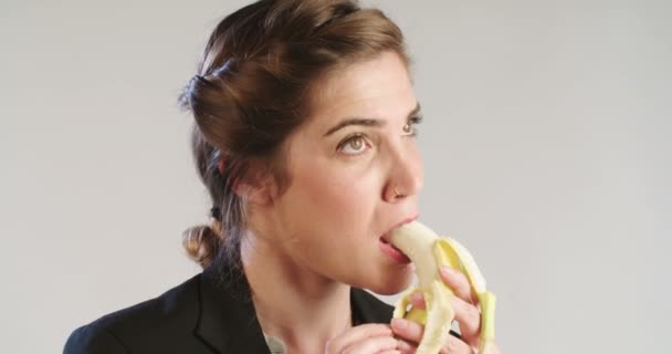 Gros plan d'une femme mangeant une banane sur fond de studio blanc — Video