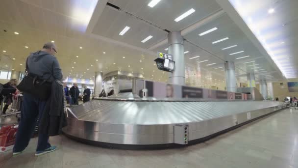 Пассажиры, собирающие багаж с транспортерной ленты в аэропорту — стоковое видео