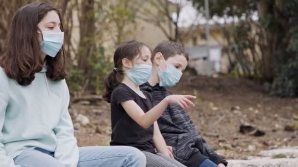 Coronavirus pandemie - kinderen dragen gezichtsmaskers om besmetting te voorkomen zittend verveeld — Stockvideo