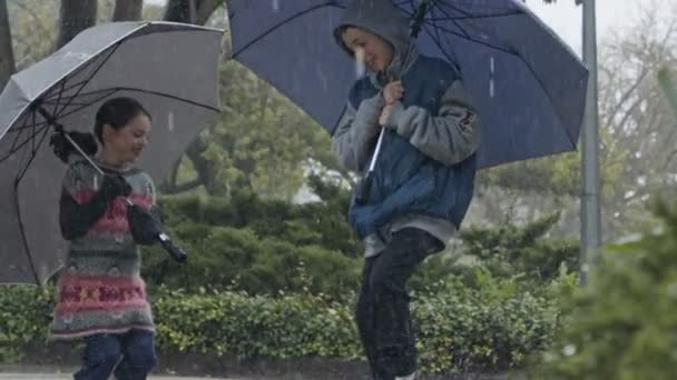 Pojke och flicka hoppar med paraplyer i ösregnet i slow motion — Stockvideo