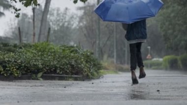 Elinde şemsiyeyle yağmurun altında atlayan genç bir çocuğun ağır çekimde
