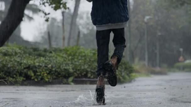 Zeitlupe eines kleinen Jungen, der im strömenden Regen springt und einen Regenschirm hält — Stockvideo