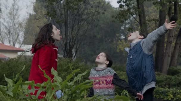 Trójka dzieci stojących i cieszących się deszczem w zwolnionym tempie — Wideo stockowe