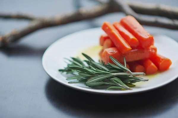 Closeup of boiled carrots, cut into cubes, a honey-creamy sauce with branches of rosemary on white plate gray blurred background. Selective focus. Concept - delicious, healthy food.