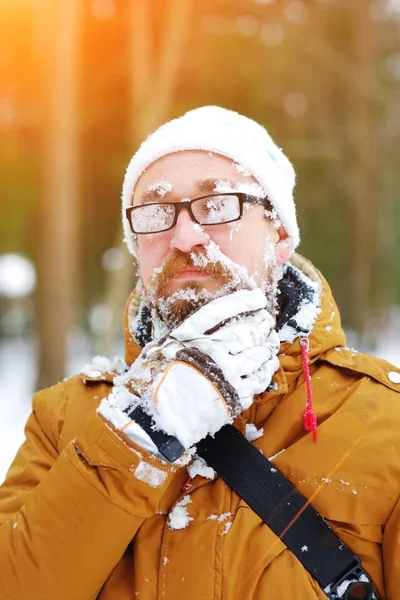 Portret młodego mężczyzny Brodaty zamrożone w Blizzard w lesie. Twarz i okulary pokryte śniegiem. On ma płatki śniegu z jego broda. — Zdjęcie stockowe
