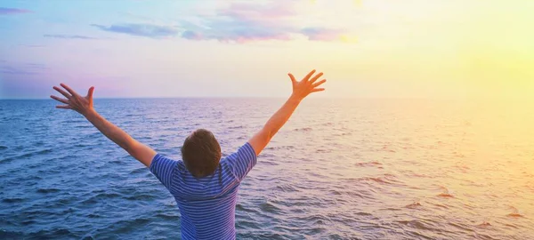 Buon uomo di preghiera a braccia aperte. Tramonto mare e nuvole nel cielo azzurro mattutino. Adorazione cristiana lode a Dio, libertà finanziaria vita speranza vittoria entusiasmo mentale salute concetto banner — Foto Stock