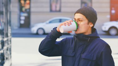 Yakışıklı, rahat giyimli, gözlük takan ve şapka tutan bir genç.