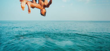 Gün batımında uçurumdan mavi okyanusa atlayan genç bir adam. Aktif açık hava, tatil macerası, turizm, sağlıklı yaz eğlencesi, eğlenceli aktivite yaşam tarzı. Mayo giyen çılgın yetişkin adam tırmanıştan uçar.