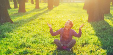 Yaz parkında yeşil çimlerde oturan mutlu genç adam, gün batımı doğa. Sakin güneş ışığına bak. Yakın göz. Huzurlu insanlar vücut rahatlığı, erkek akıl sağlığı, bedava yoga adamı, insan hayatı zen konsepti. Akşam bahçesi yüzü, hayal kuran ruh iyimserliğinin keyfini çıkar.