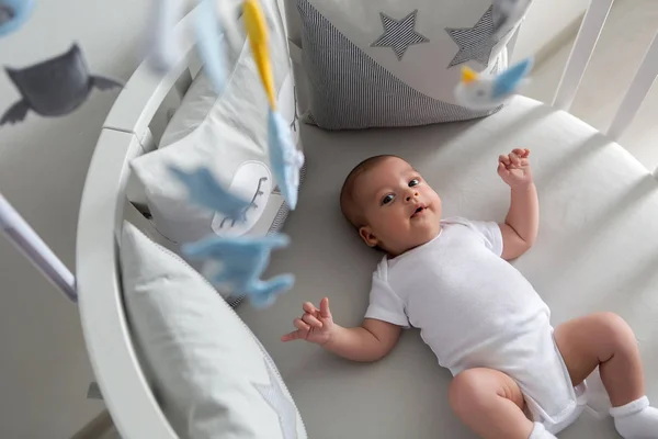 newborn lies in the round white bed with mobile