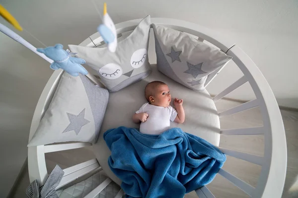 newborn lies in the round white bed with mobile