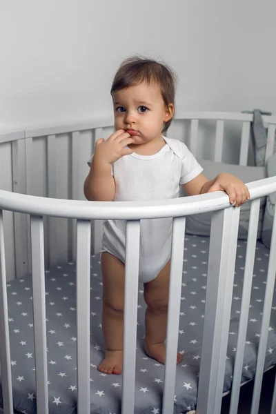 one year old child in white clothes standing in a white round bed