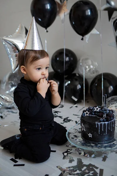 boy stands next to a festive black cake