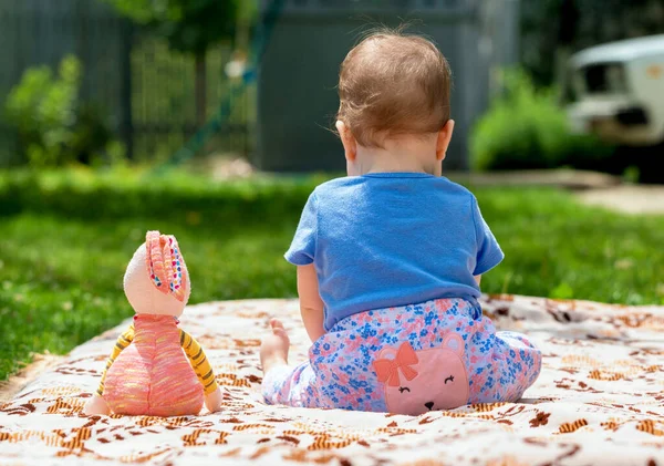 Küçük bir çocuk bir oyuncakla yatak örtüsüne oturur. Çıplak ayaklı bir çocuk. Güneşli yaz günü