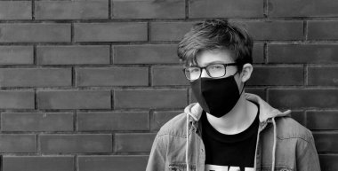 Siyah koruyucu maskeli genç adam. Koyu gri arka planda siyah bir tıbbi maske takmış hevesli birinin portresi. Yüzünde siyah maske olan bir adam. Cowid-19 salgını.