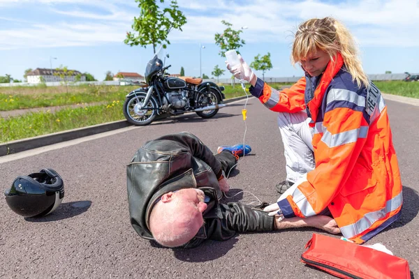 一位德国急救人员帮助受伤的摩托车司机 Rettungsdienst 是德国的救护车服务词 — 图库照片