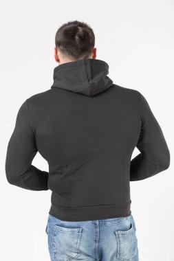 Siyah kapüşonlu ve beyaz arka planda kot pantolon giyen bir adam.