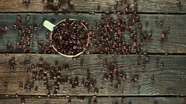 Grãos de café Arabica cair em uma caneca transparente em um piso de madeira . — Vídeo de Stock