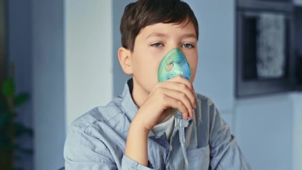 Tratamiento para el asma, el niño respira a través de un inhalador. De pie en la cocina — Vídeo de stock