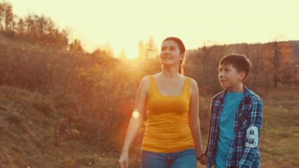 Mãe e filho caminham juntos na grama do gramado com uma bela luz do pôr do sol, sentindo amor vida familiar — Vídeo de Stock