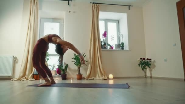 Pretty female yoga instructor is demonstrating body twists, stretching then relaxing with hands on knees and breathing. — Stock Video