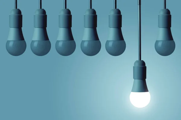 LED lambası yanıyor ve diğer ampuller koyu mavi arka planda parlamıyor. Yaratıcılık kavramı.