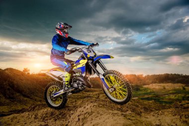 Profesyonel motosiklet sürücüsünün dağlarda sürüşünün ve off-road yolunda ilerleyişinin yan görüntüsü. Gün batımı..