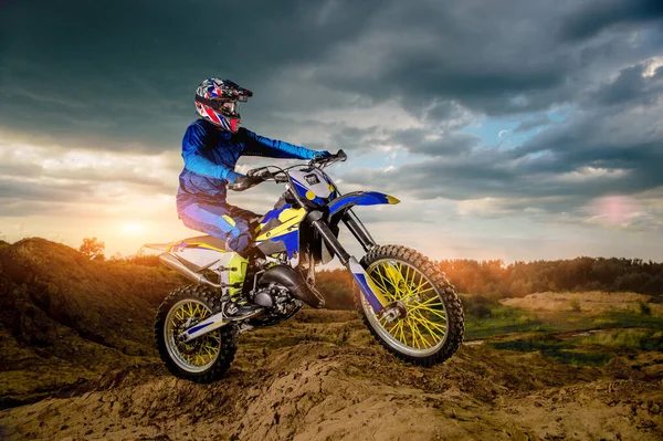 Profesyonel motosiklet sürücüsünün dağlarda sürüşünün ve off-road yolunda ilerleyişinin yan görüntüsü. Gün batımı..