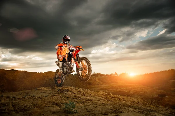 Profesyonel motosiklet sürücüsünün dağlarda ve off-road yolunda ilerleyişinin yan görüntüsü. Gün batımı..