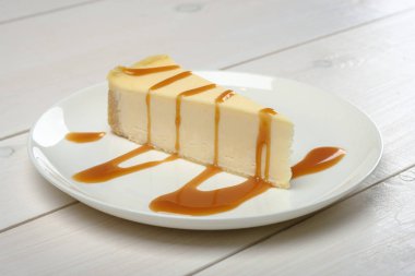 bir parçası cheesecake, drizzled üzerinde ahşap beyaz masa üzerinde beyaz tabak duran Karamel Sos.