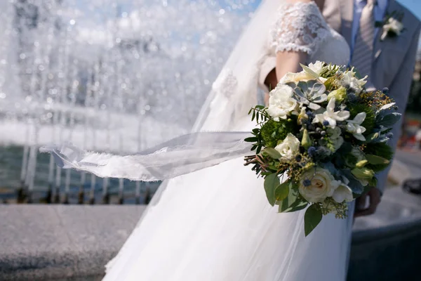 Groene en witte bruiloft boeket in handen van de bruid met een wapperen in de wind blue lace lint — Stockfoto