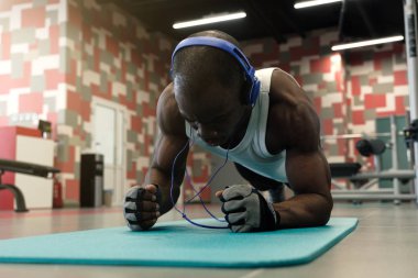 Kendine güvenen kaslı genç adam yerde egzersiz yaparken spor giyim ve iş tahta pozisyonu giyiyor