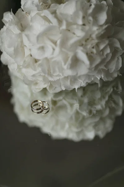 Een boeket van witte hortensia's en verlovingsringen liggen op een glazen tafel. Close-up verticale foto — Stockfoto