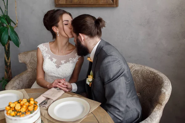 The bride and groom are sitting at the table at the table. The bride is kissing the groom on the forehead