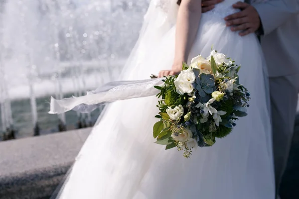 Groene en witte bruiloft boeket in handen van de bruid met een wapperen in de wind blue lace lint — Stockfoto