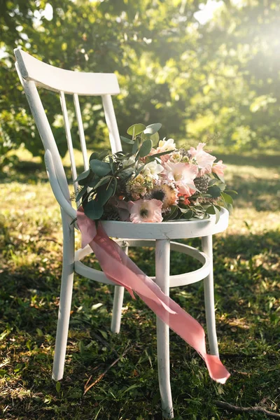 Ramo nupcial de flores rosadas y vegetación con cinta, se encuentra en la silla de madera blanca vintage — Foto de Stock