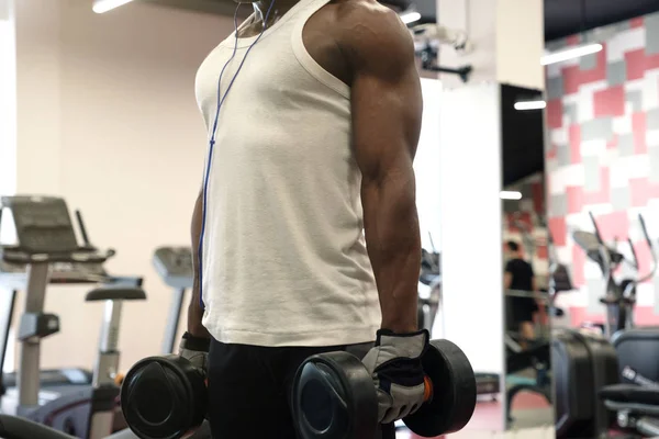 Musculoso hombre negro en una camiseta blanca haciendo ejercicios con pesas en el gimnasio — Foto de Stock