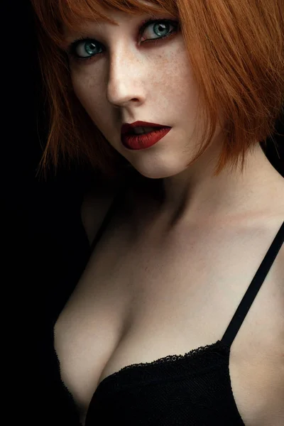 Porträt eines jungen Mädchens mit roten Haaren und Sommersprossen mit roten Lippen und blauen Augen mit dunklem Make-up, das in die Kamera blickt — Stockfoto