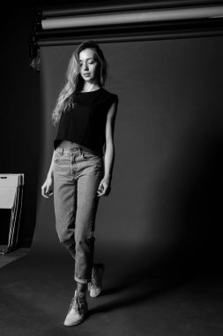 Sarışın kız t-shirt ve kot adım modeli testler yapma karanlık bir arka plan siyah beyaz portre.