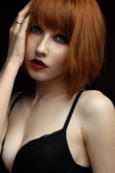 Portrét mladé rusovláska v černou podprsenku s tmavého makeupu a červené rty při pohledu do kamery — Stock fotografie
